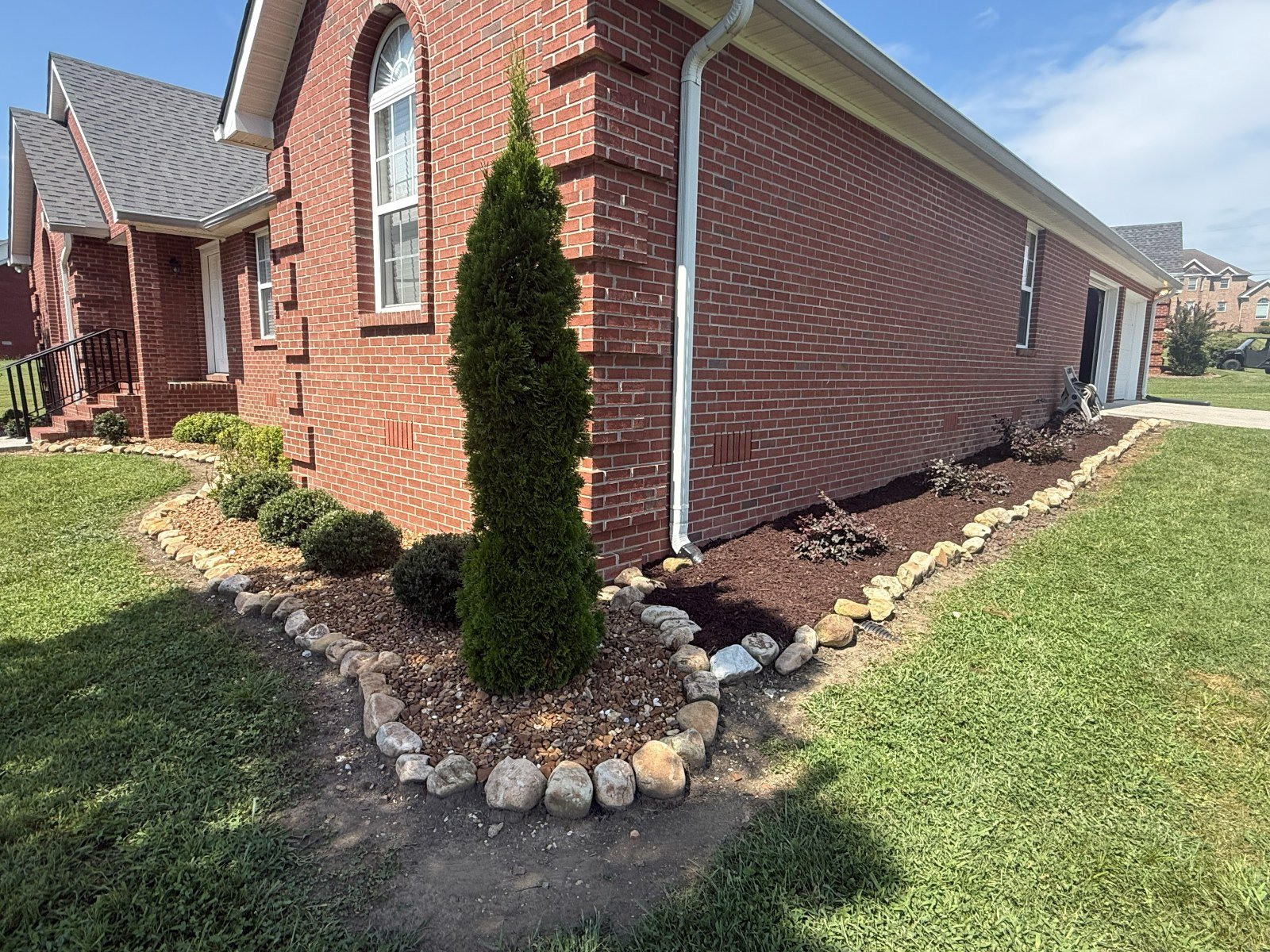 Rock-bordered mulch bed with arborvitae and boxwood
